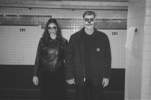 Husband and wife in the subway wearing all black and skeleton face
        paint staring unnervingly into the camera