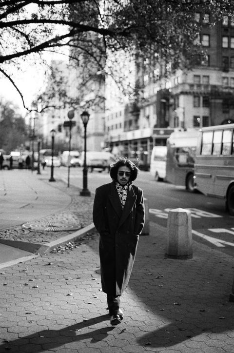 Stylish looking man complete with overcoat, earmuffs, sunglasses,
        and mustache walks through the park